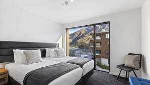 A modern hotel room with a large bed, a small desk, and a view of mountains through a sliding door. - Residence Du Parc - Awa Apt 16a (Arthurs Point)
