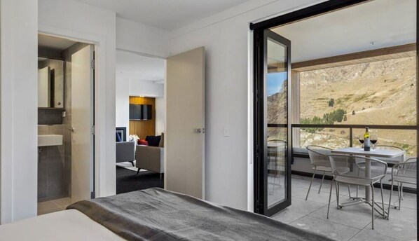 A modern hotel room with a balcony, a bed, a seating area, and a view of the outdoors.