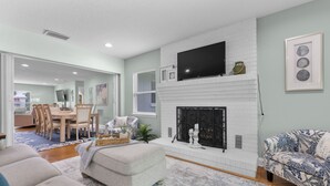 A living room with a fireplace, a television mounted above it, and a dining area with a table and chairs. - Pool and Hot Tub Home with Pickle Ball Court and Walk to Downtown (St. Augustine)