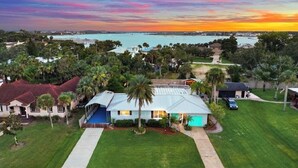 A residential area with a house featuring a covered porch, a swimming pool, and a view of a body of water during sunset. - Pool and Hot Tub Home with Pickle Ball Court and Walk to Downtown (St. Augustine)