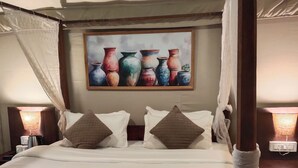 A four-poster bed with white linens and two pillows, a painting of vases on the wall, and bedside lamps. - Goya Gate Beach Resort (Arambol)