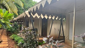 A covered outdoor area with a series of tents, a dirt pathway, and various plants. - Goya Gate Beach Resort (Arambol)
