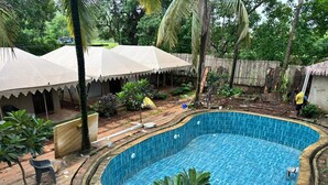 A swimming pool with a wooden deck surrounding it, a covered seating area, and lush greenery. - Goya Gate Beach Resort (Arambol)