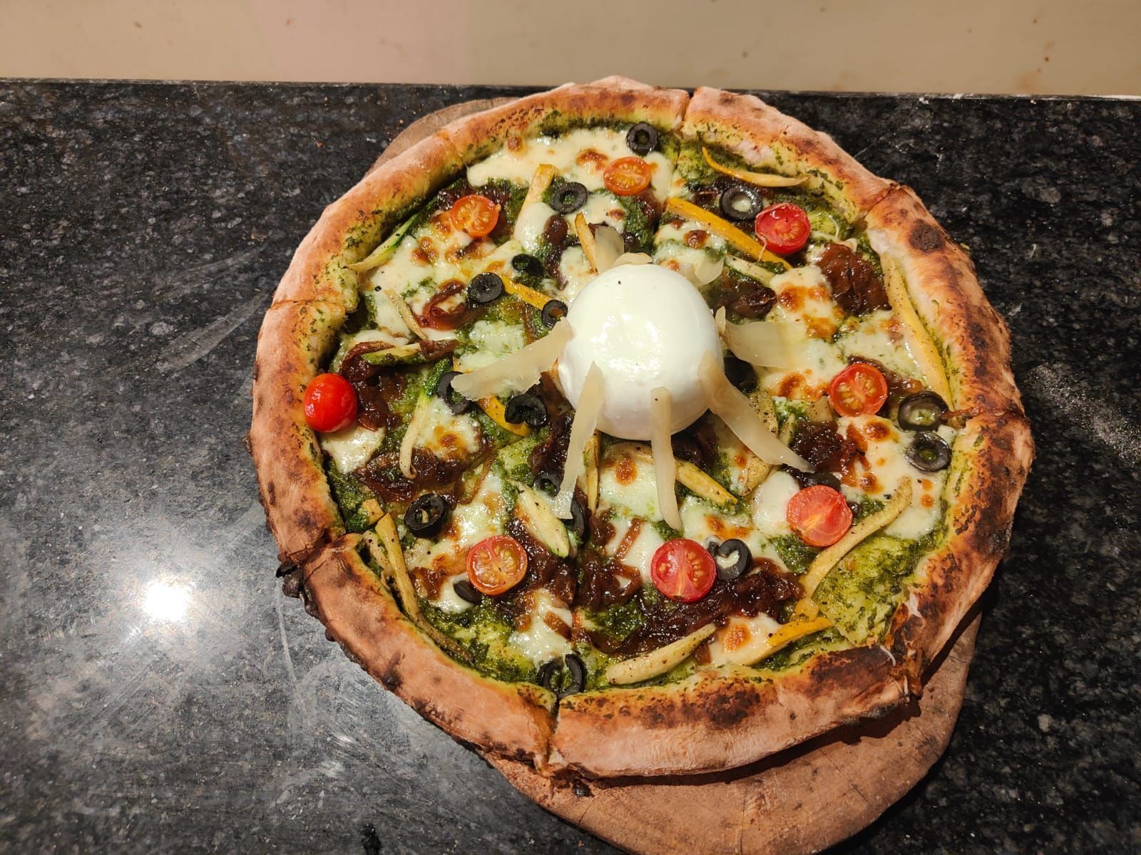 Una pizza con distintos ingredientes sobre una encimera negra.