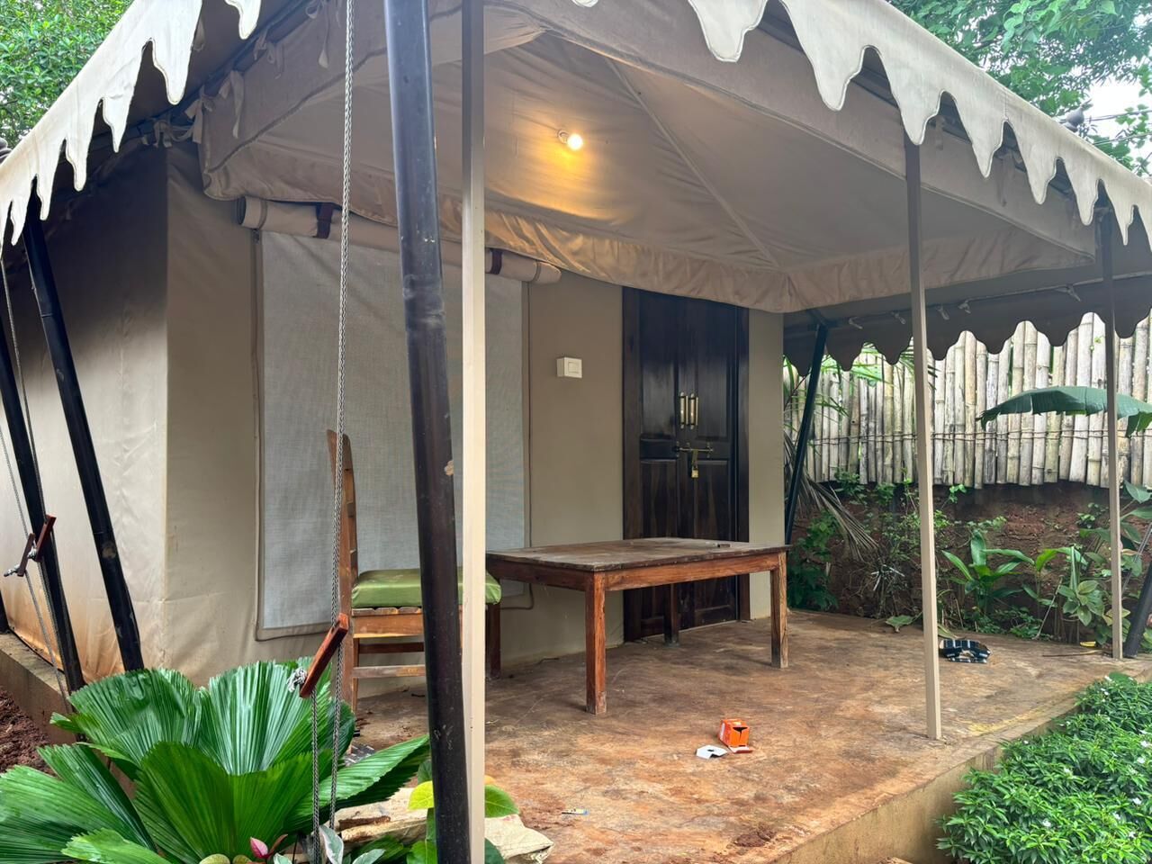 A tent with a table and chairs, surrounded by greenery.