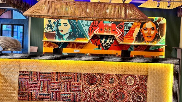 A reception area with a woven ceiling, vibrant artwork, and a patterned carpet. - Goya Gate Beach Resort (Arambol)