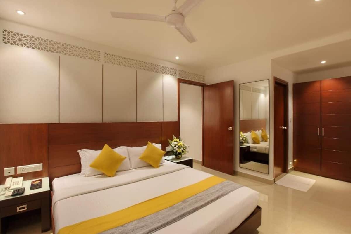 Una habitación de hotel con cama, mesita de noche, espejo, armario y ventilador de techo.