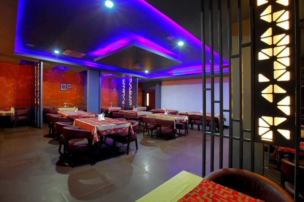 Un restaurant avec des tables dressées pour le service, un coin bar et un mur décoratif orné de motifs géométriques.