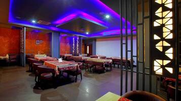 Un restaurant avec des tables dressées pour le service, un coin bar et un mur décoratif orné de motifs géométriques.