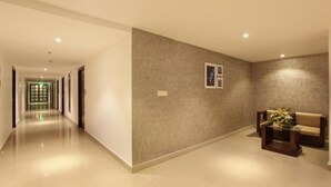 Un couloir d’hôtel avec un espace de réception, un canapé et une petite table sur laquelle se trouve un vase.