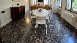 A spacious room with a marble floor, a round dining table with chairs, a sofa set, a TV mounted on the wall, and large windows. - madoneta apartment (Venice)