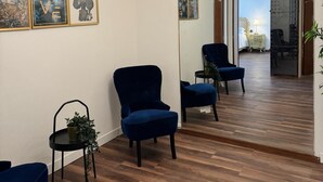 A modern interior with a wooden floor, blue armchairs, and a mirror reflecting the room. There are framed artworks on the wall and a ceiling light fixture. - madoneta apartment (Venice)