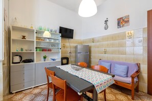 Een kleine keuken met een eettafel, stoelen, een bank en een koelkast.