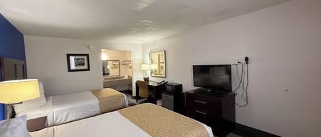 A hotel room with two beds, a desk, a TV, and a mirror.