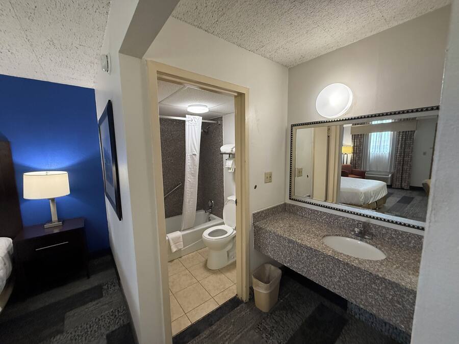 A hotel bathroom with a shower, toilet, sink, and a large mirror.