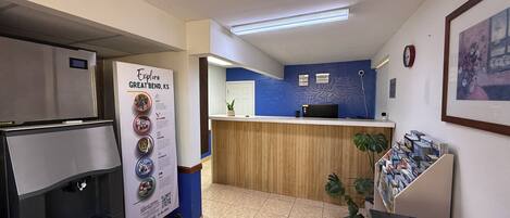 Zona de recepción con mostrador de madera, refrigerador, dispensador de agua y un cartel.
