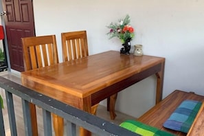 A wooden dining table with chairs, a vase with flowers, and a small table with a cushion.
