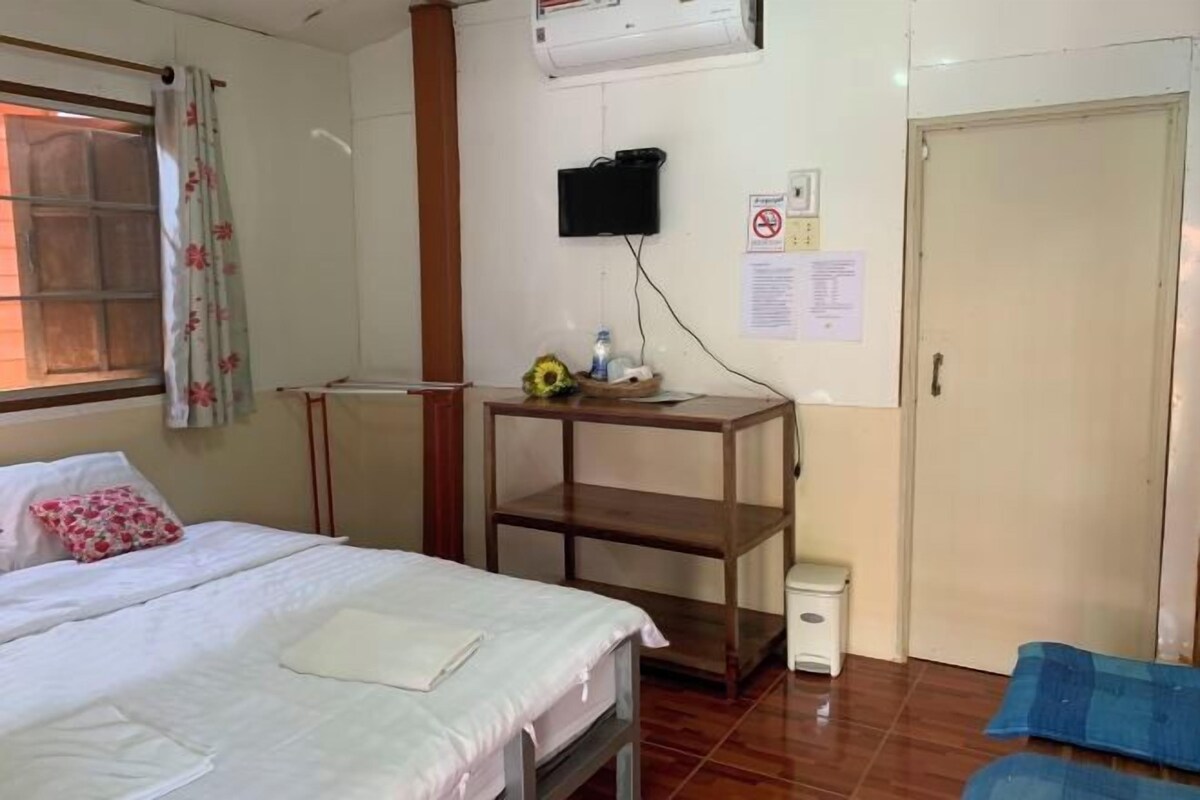 A hotel room with a bed, a small table with a vase, a TV mounted on the wall, and a door.