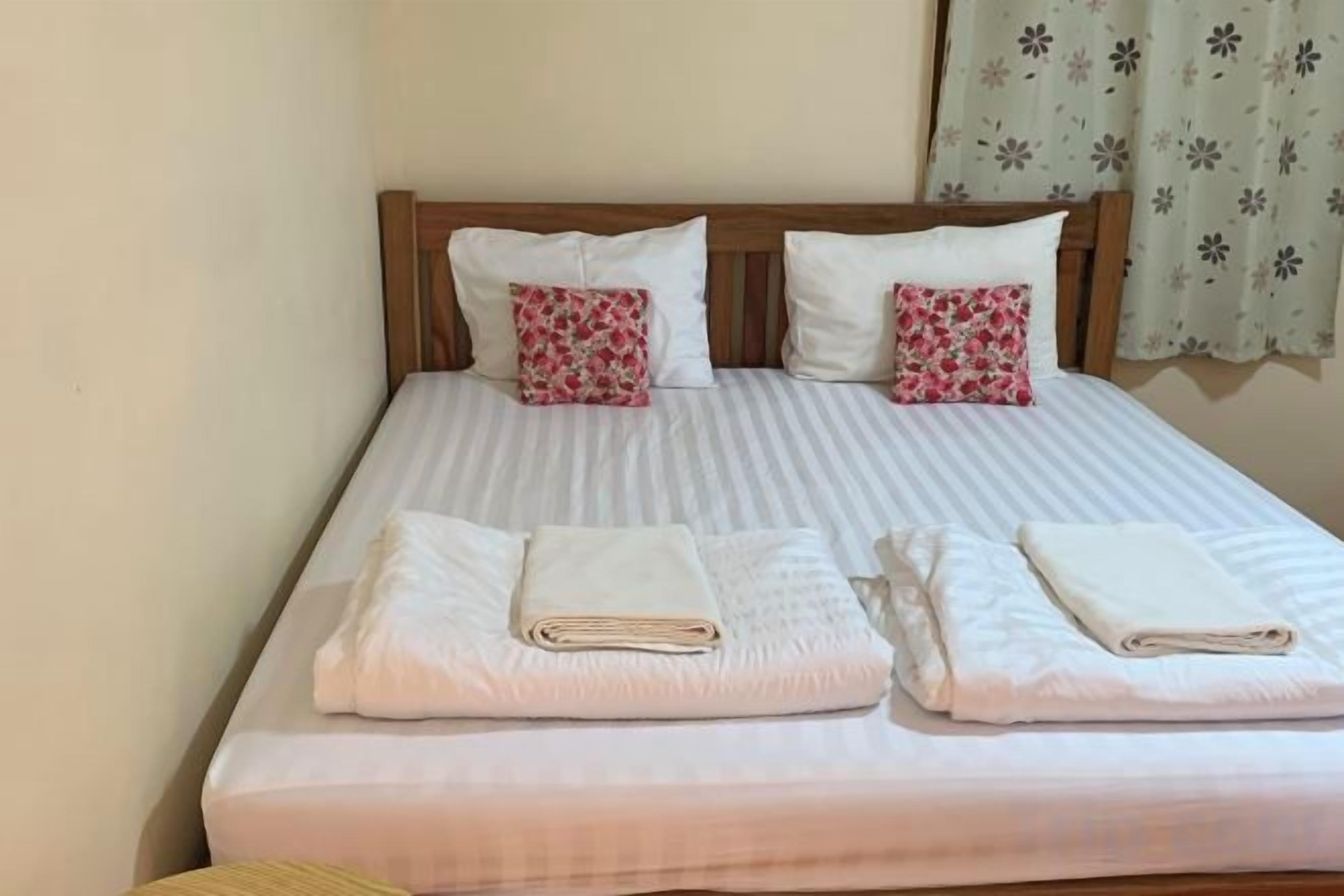 A double bed with two pillows, a wooden headboard, and a window with curtains.