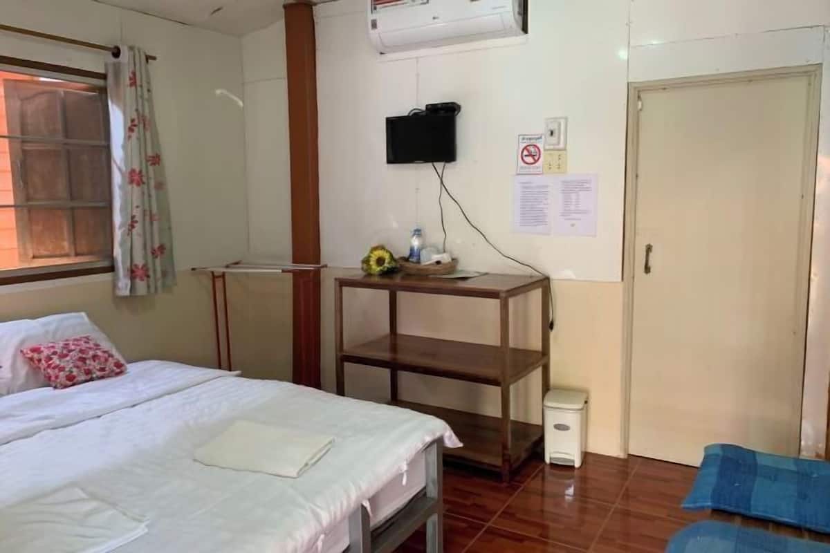 Une chambre d’hôtel avec un lit, une petite table sur laquelle se trouve un vase, un téléviseur fixé au mur et une porte.