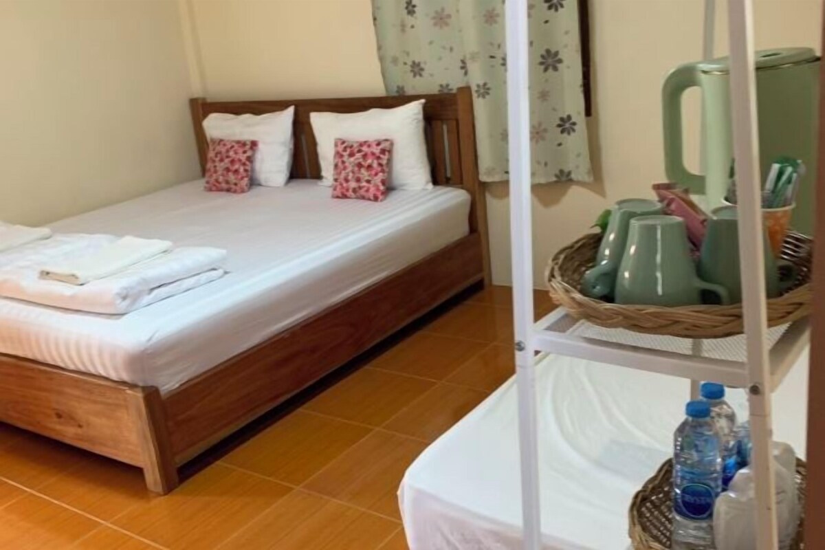 A single bed with a wooden frame, a white mattress, and two pillows. There is a wicker basket on the floor beside the bed.