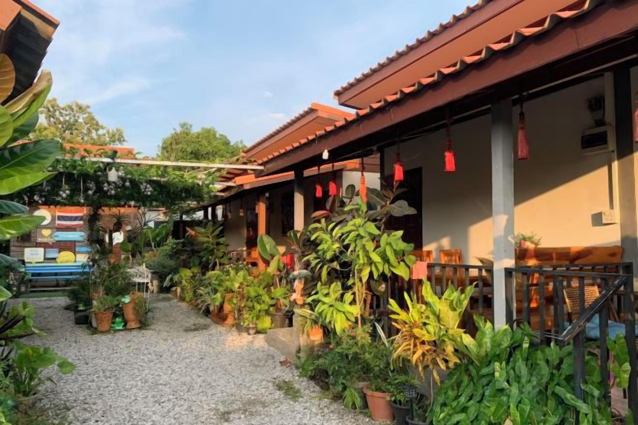 A building with a red-tiled roof, a gravel pathway, and various potted plants.