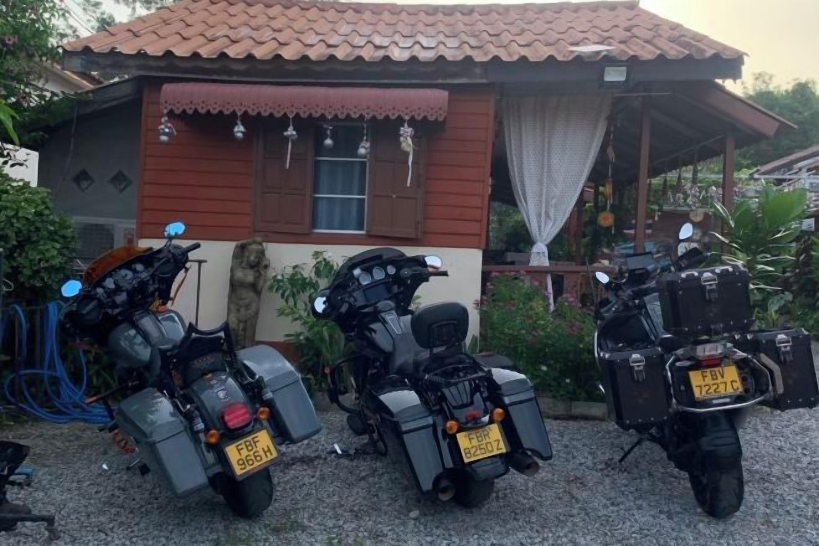 Two motorcycles parked in front of a house with a tiled roof and a small porch.