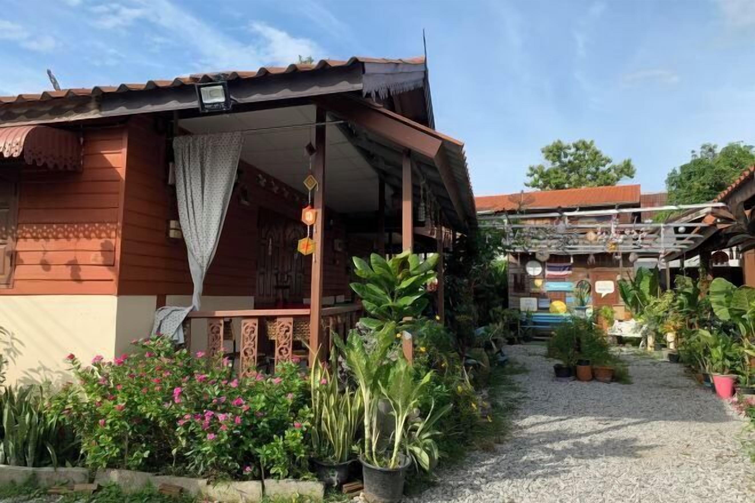 A traditional wooden house with a porch, surrounded by potted plants and a gravel path.