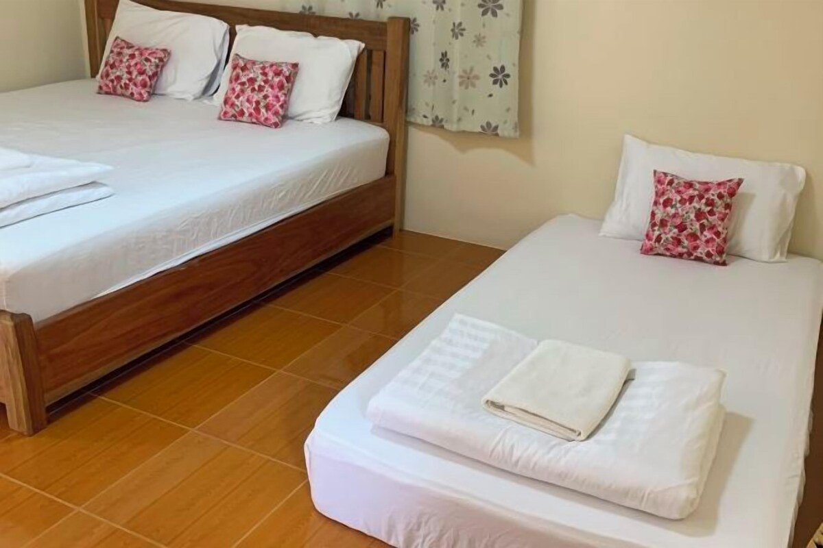 Habitación de hotel con dos camas, cada una con ropa de cama blanca y almohadillas florales rosadas.
