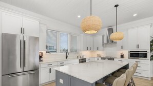 A modern kitchen with white cabinetry, a large island, stainless steel appliances, and a hanging woven light fixture. - 5350 Chasing Sunshine: 5bd/4.5ba Pool Home! 5 Bedroom Home (Fort Myers Beach)