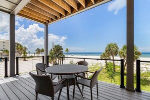 A covered outdoor area with a table and chairs, overlooking a beach with palm trees and a clear sky. - 5350 Chasing Sunshine: 5bd/4.5ba Pool Home! 5 Bedroom Home (Fort Myers Beach)