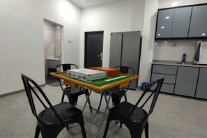 Una habitación pequeña y moderna con una mesa de comedor, cuatro sillas y una kitchenette con armarios y un refrigerador.