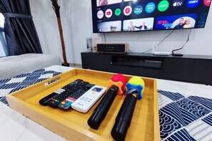 A tray with remote controls, a TV remote, and a pair of headphones on a bed with a patterned bedspread. - UjongPasir ModenHouse - Karaok/MsgChair/ArcadeGame (Melaka)