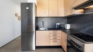 A modern kitchen with a stainless steel refrigerator, wooden cabinets, a black countertop, a microwave, and a stove. - Vacation 'Casa Tagoro Dream' with Shared Pool, Private Terrace and Wi-Fi (Costa del Silencio)