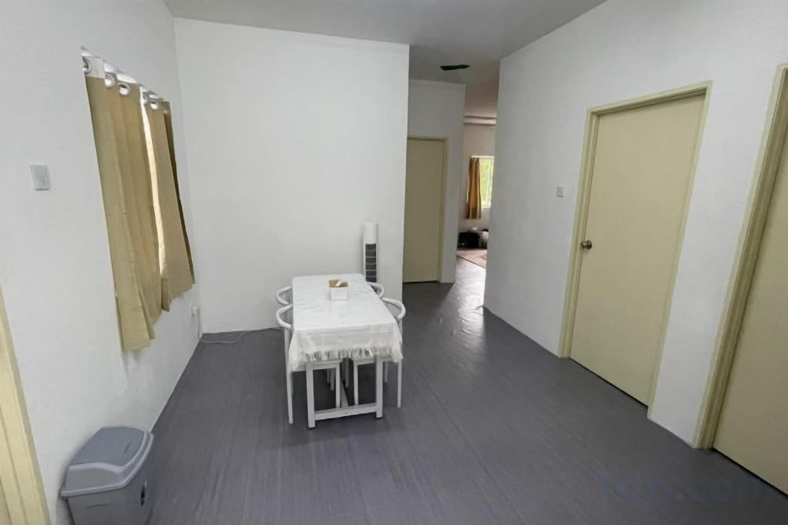 A hallway with a white table and chairs, a trash bin, and a door.