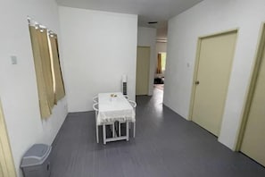 A hallway with a white table and chairs, a trash bin, and a door. - Oryza Panthera Cottage (Api-Api)