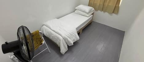Una habitación pequeña con cama, ventilador y ventana con cortinas.