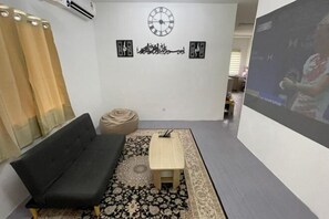 Egy szoba, melyben egy fekete kanapé, egy kis, fából készült asztal, egy mintás szőnyeg, egy óra és két díszes falfelület található.