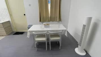 A small room with a white table and chairs, a window with curtains, and a standing heater.