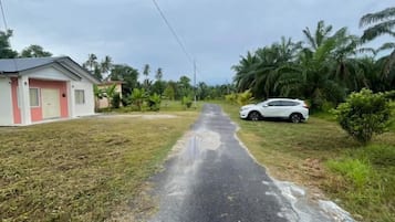 A paved road leading to a residential area with houses and a white car parked on the side.