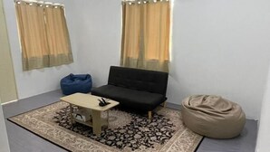 Ein kleiner, moderner Raum mit einer schwarzen Couch, einem kleinen Tisch, einem Sitzsack und einem gemusterten Teppich.
