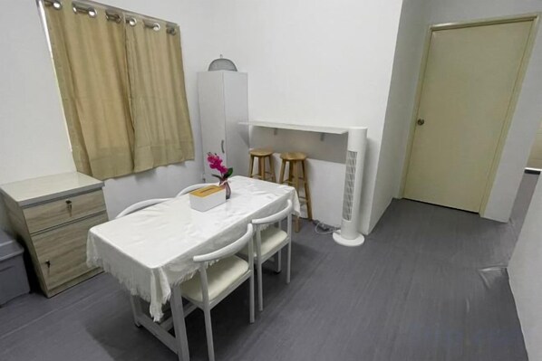 Une petite pièce propre, avec un lit, une table de chevet et un bureau avec deux chaises. Il y a une fenêtre avec des rideaux, une porte et un radiateur.
