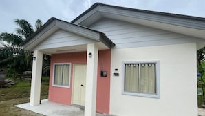 Ein zweistöckiges Haus mit rosa und weißen Fassade, einer Veranda und einem kleinen Fenster.