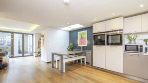A modern kitchen with white cabinets, a dining area with a bench, and a large window providing natural light. - Spacious, Canal-Side, 3bed flat (London)
