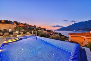 A rooftop infinity pool with a view of a coastal town at dusk. - Villa Basil Amazing Sea view (Antalya)
