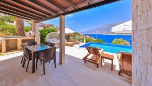 Eine Außenpatio mit Pool, Essbereich und Liegestühlen mit Blick auf eine malerische Küstenlinie.