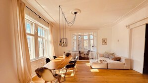 A spacious living area with a wooden floor, a dining table with chairs, a sofa, and a window with curtains. - "Villa Suite" Spacious old villa with terrace near Stuttgart (Aidlingen)