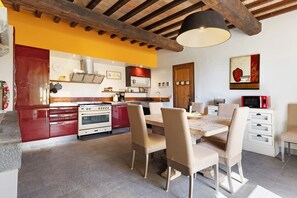 Une cuisine avec des meubles de couleur rouge, des appareils électroménagers blancs et un coin repas avec des chaises beiges et une table en bois.