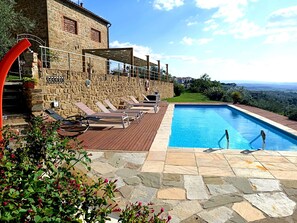 Un bâtiment en pierre doté d’une piscine, de chaises longues et offrant une vue sur le paysage.