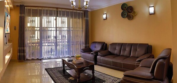 A living room with a brown leather sofa, a coffee table, and a patterned rug. - Karay Apartments (Kampala)